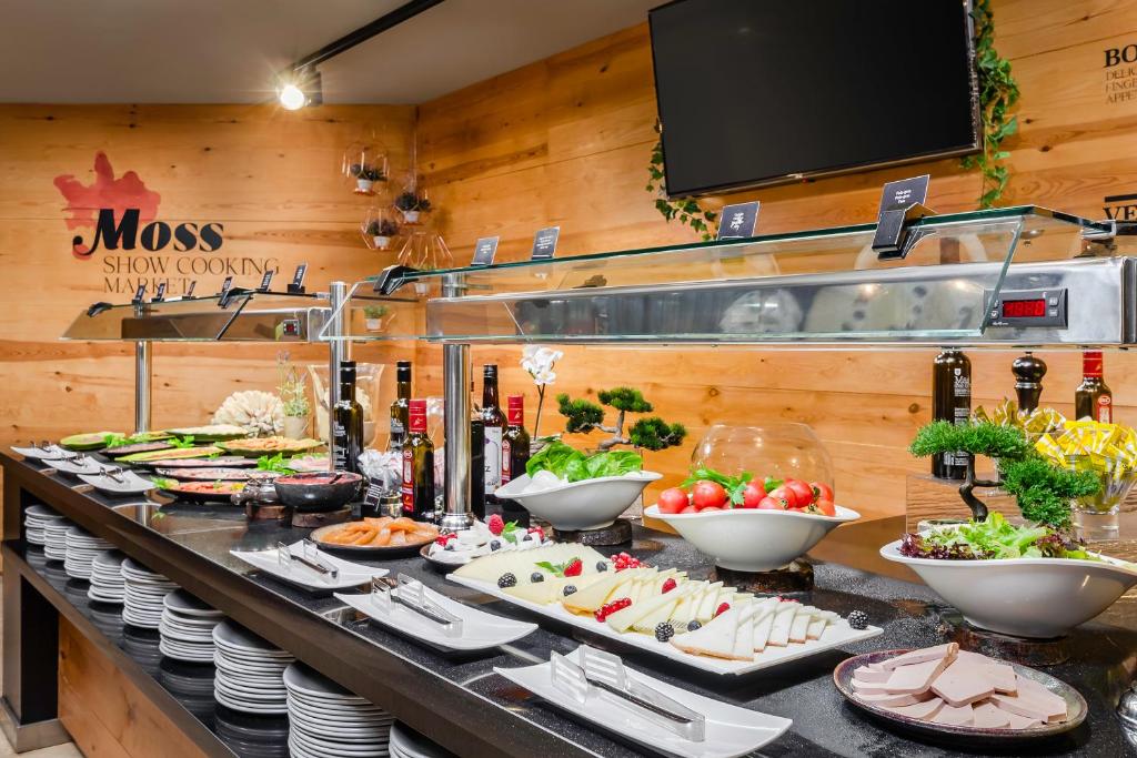 Bufete ar dažādiem ēdieniem, tostarp salātiem, sieriem un gaļas izstrādājumiem, piedāvātais ēdiens ir sakārtots pie elegantas koka sienas.