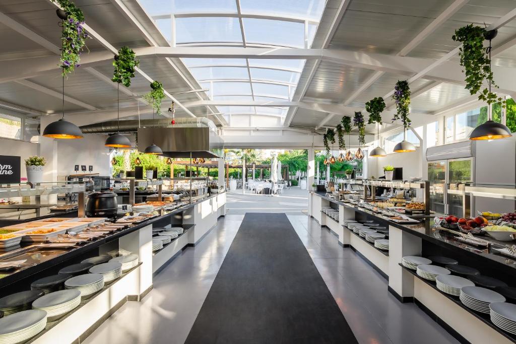 Mūsdienīga un gaiša ēdienu pasniegšanas zona ar bufeti, dekorēta ar zaļumiem un stilīgām lampām. Telpa ir atvērta, ļaujot ieplūst dabiskajai gaismai un radot patīkamu atmosfēru.