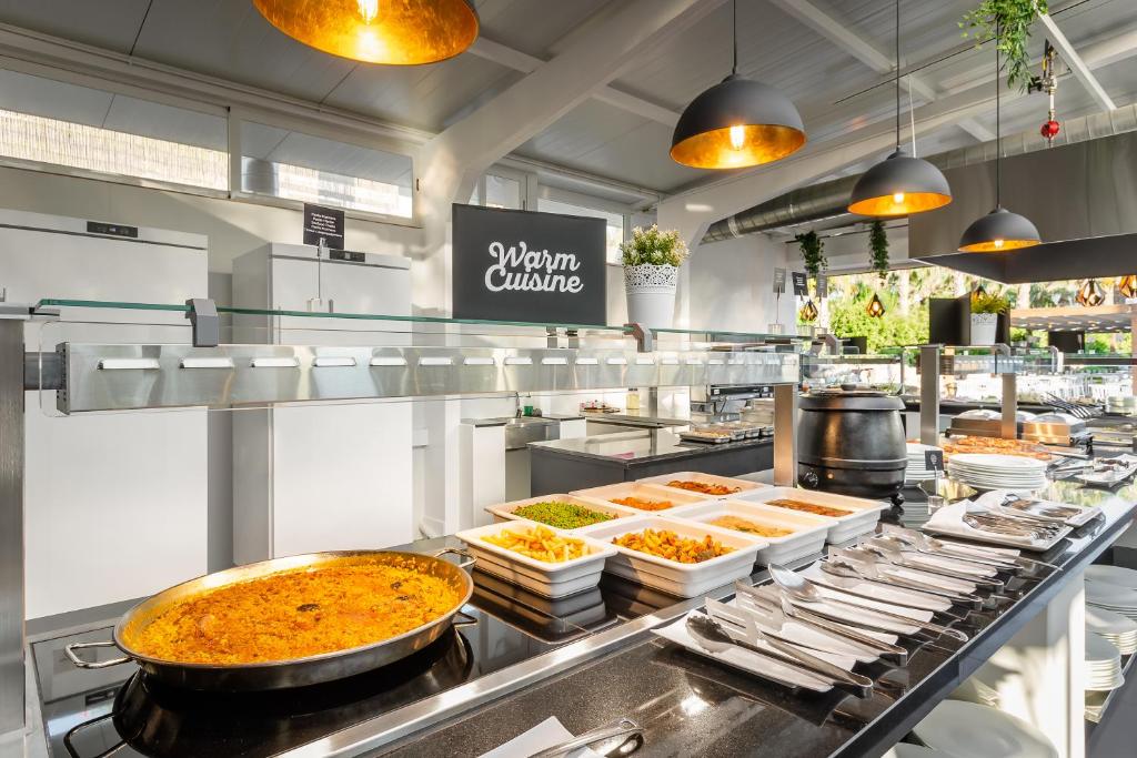 Siltas virtuves bufete ar daudzveidīgiem ēdieniem, kas izvietoti uz elegantas galda virsmas. Gaismas piekariņi un augi piešķir patīkamu atmosfēru.