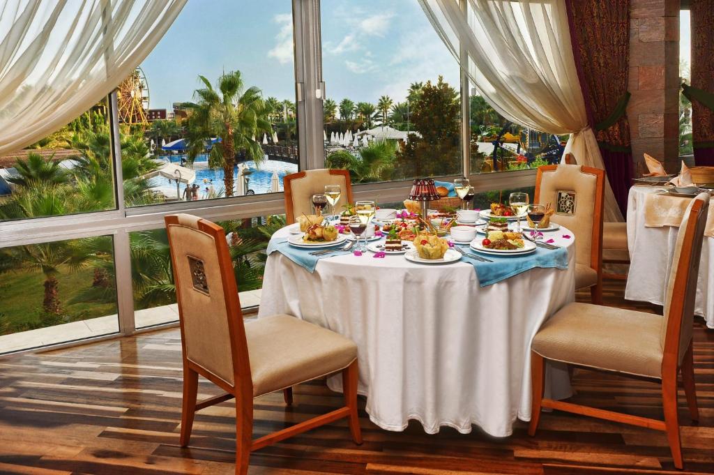 Elegantā restorāna galds ar gourmet ēdieniem un dzērieniem, skats uz peldbaseinu un tropisko ainavu.
