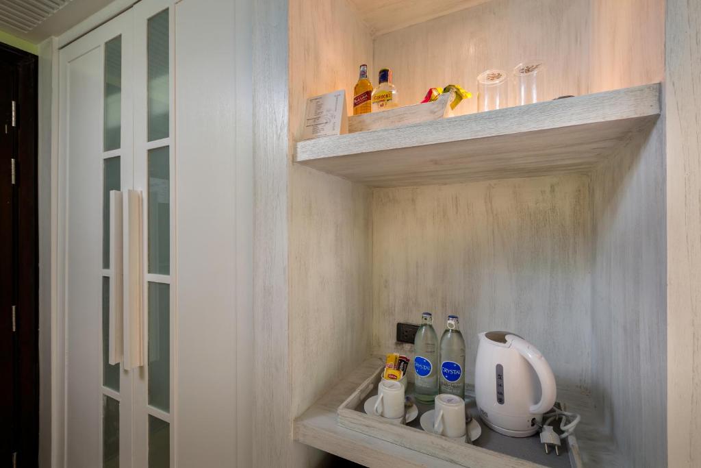 Kafijas stūra skats ar ūdens pudelēm, elektrisko kettle un glāzēm, kas novietotas uz plauktiem viesnīcas numurā.