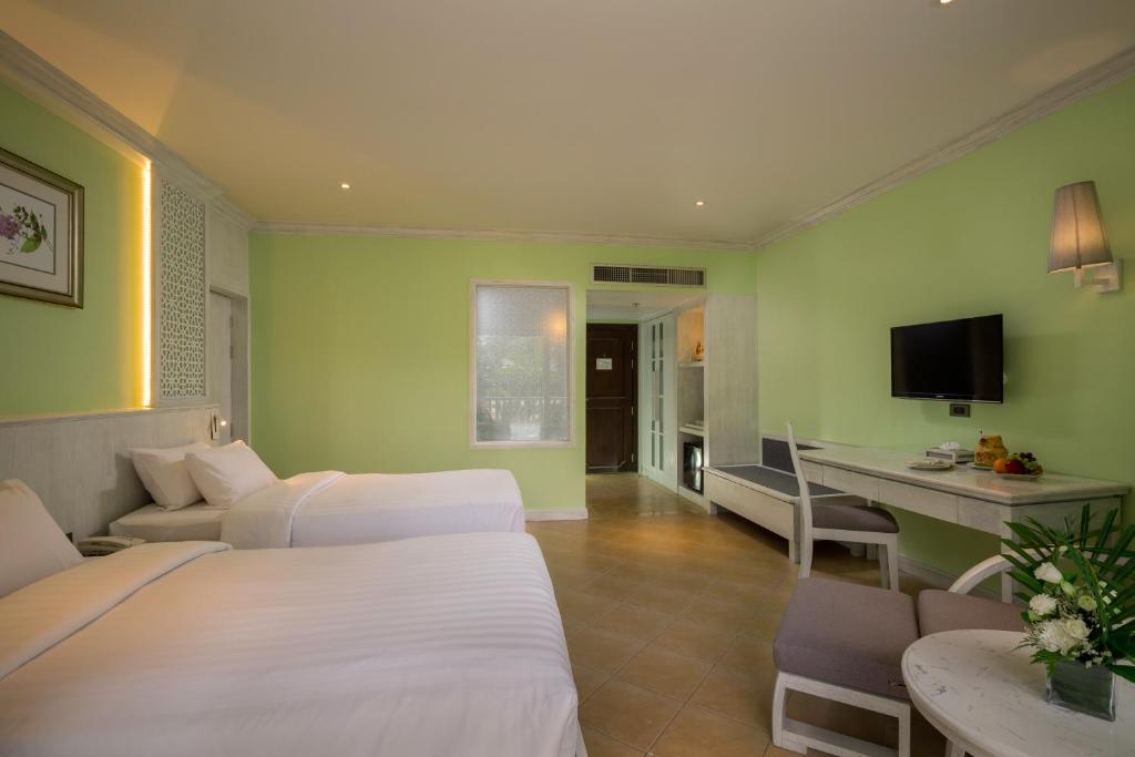 Mūsdienīgs viesnīcas numurs ar divām gultām, gaiši zaļām sienām un elegantu mēbelējumu, kas ietver televizoru un galdu. Telpa ir gaiša un gaumīga, radot patīkamu atmosfēru.