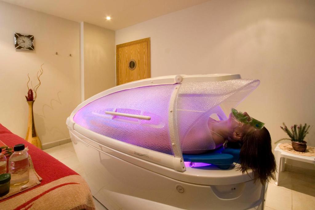 Relaksējoša spa procedūra ar krāsainu apgaismojumu un sievieti, kas atpūšas speciālā vannā. Vannā ir iekārtas, kas veicina atslābumu un labsajūtu.