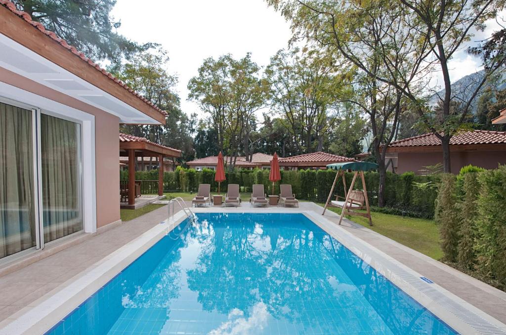 Peldbaseins ar saulessargiem un šūpolēm, ieskauts zaļumiem un mājīgām mājām, ideāla vieta atpūtai un relaksācijai.