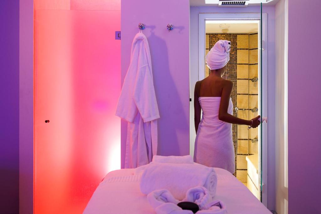 Skaista spa telpa ar relaksējošu apgaismojumu, kur sieviete, ietērpta dvielī, gatavojas ieiet dušā.