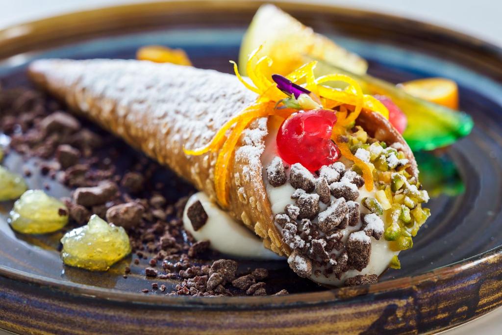 Saldētais deserts kanolī ar riekstiem, augļiem un šokolādes drupatām, dekorēts ar cukura pūderi un gurķu želeju. 