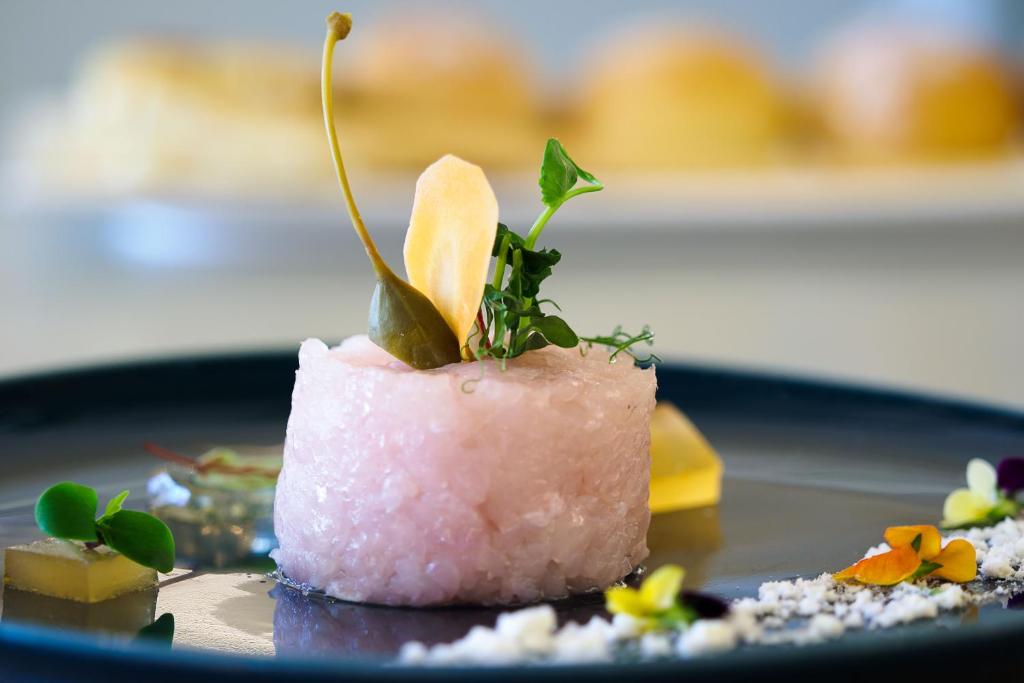 Elegants un krāsains kulinārijas šedevrs uz melnas plāksnes, kas satur rozā krāsas ēdienu ar zaļumiem un dekoratīviem elementiem. Ideāla izvēle gourmet ēdienu mīļotājiem.