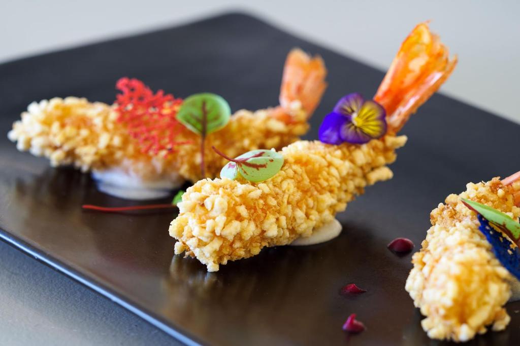 Kraukšķīgi garneles uz melna šķīvja, dekorētas ar krāsainām ziedu un augu lapu detaļām.