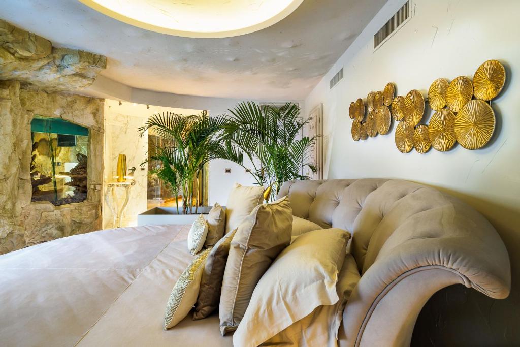 Mūsdienīgas guļamistabas interjers ar dīvānu un dekoratīvām palodzēm, kas papildina telpas eleganci. Zeltainas sienas dekorācijas un zaļie augi rada relaksējošu atmosfēru.