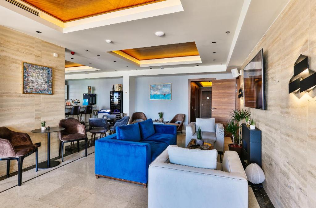 Mūsdienīgs viesnīcas viesistaba ar zilu un baltu mēbeļu kombināciju, kas rada relaksējošu atmosfēru. Interjerā ir redzami mākslas darbi un augu akcenti, kas papildina kopējo dizainu.