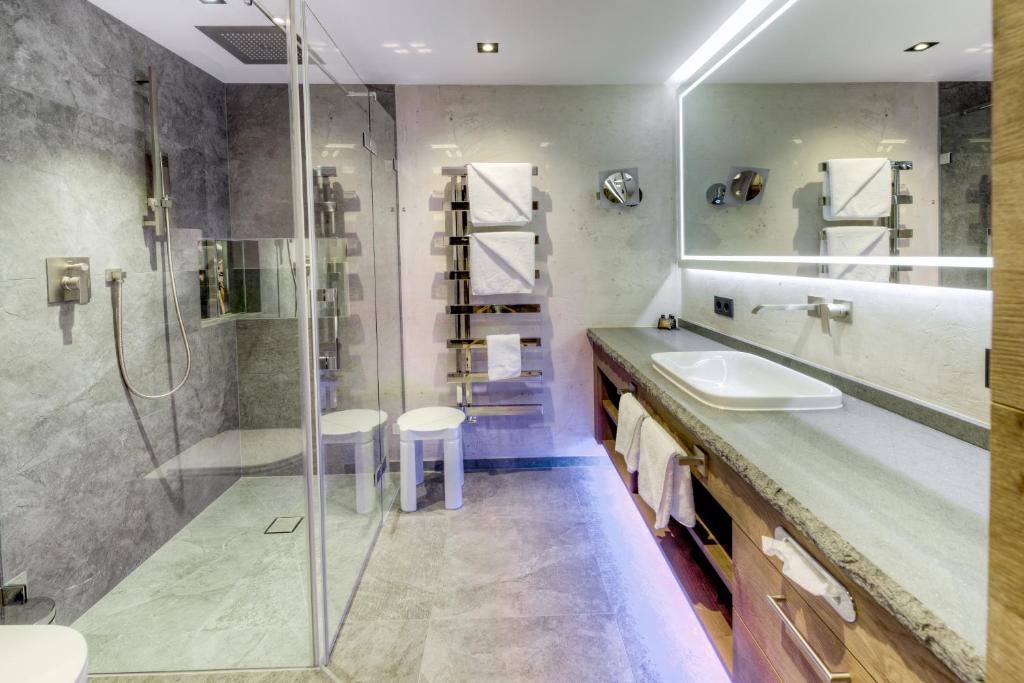 Moderns un elegants vannas istabas interjers ar stikla dušu, akmens izskata flīzēm un mūsdienīgu apgaismojumu. Vannas istabā ir arī eleganta izlietne un glabāšanas risinājumi.