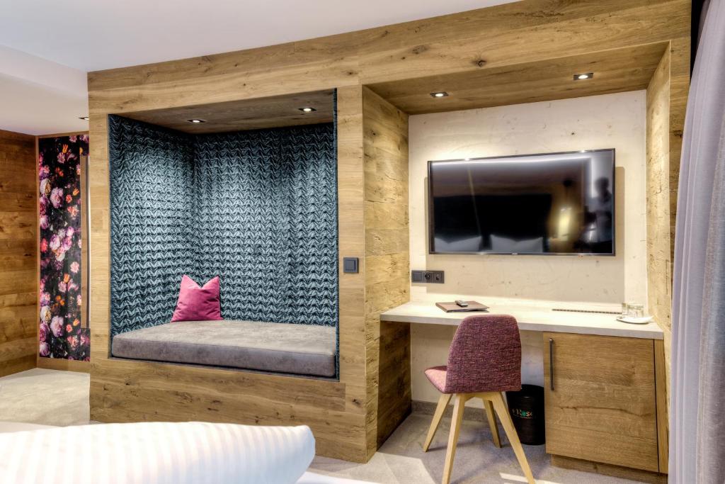 Mūsdienīga viesnīcas numura iekārtojums ar koka apdari, ērtu sēdvietu un televizoru. Telpā ir stilīgi aksesuāri un krāšņi ziedu tapetes.