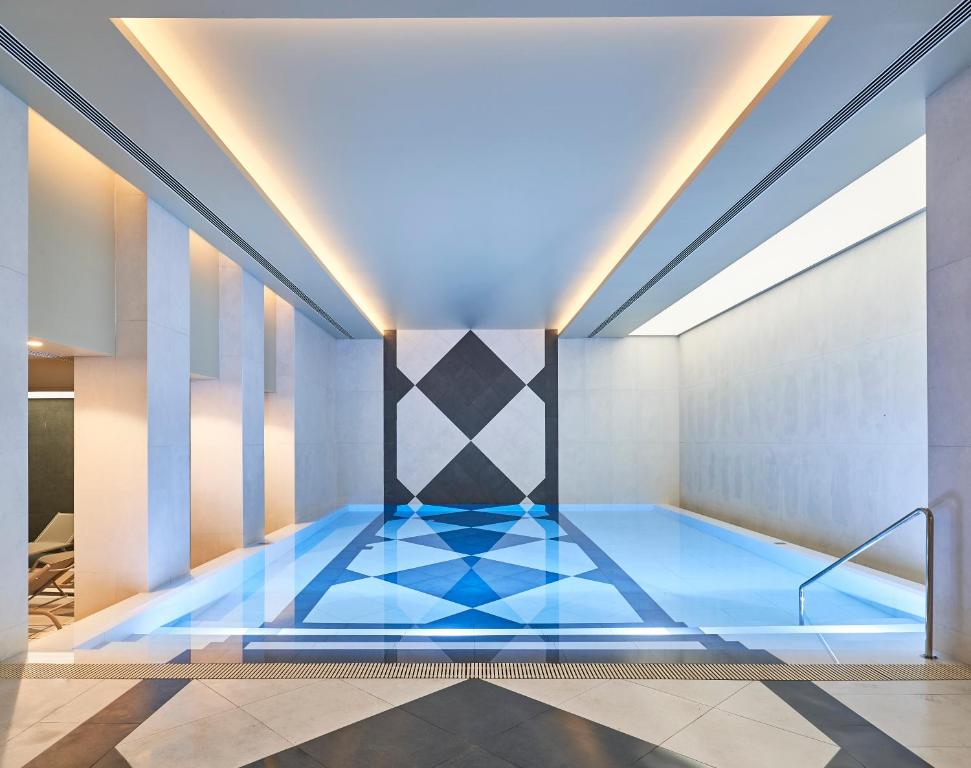 Mūsdienīgs iekštelpu peldbaseins ar ģeometrisku dizainu un spilgtu apgaismojumu, radot relaksējošu atmosfēru. Peldbaseina ūdens ir skaidrs un atspoguļo eleganto apkārtni.