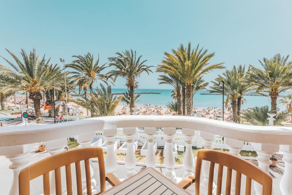 Skats no balkona uz pludmali, palmām un jūru, radot relaksējošu atpūtas atmosfēru. Ideāls attēls vasaras brīvdienām.