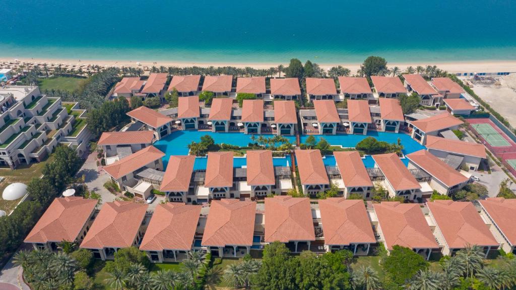 Viesnīcas kompleksa skats no augšas, kurā redzami mājiņas apbaseinā un blakus pludmalei ar kristāldzidru ūdeni. Apkārt ir zaļi koki un peldēšanas vietas, radot relaksējošu atmosfēru.