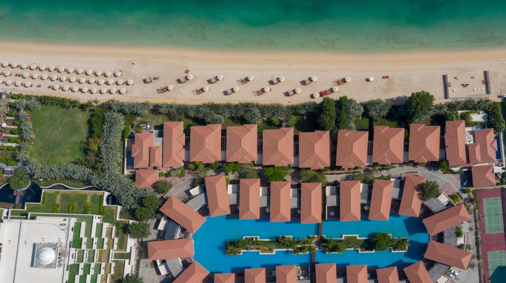 Apskate no gaisa uz piekrastes kūrortu, kur redzami viesnīcu kompleksi, baseini un pludmales gultas, kā arī skaidra zila jūra un smilšu pludmale.