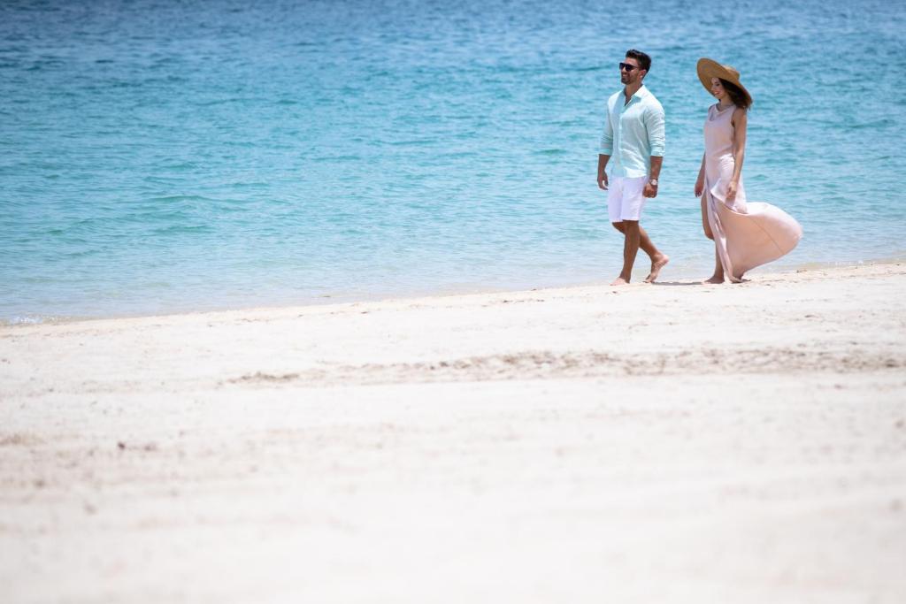 Pāris staigā pa pludmali, baudot saulainu laikapstākli un mierīgu jūru. Viņi ir ģērbušies vasaras apģērbā, kas piešķir attēlam romantisku un relaksētu noskaņu.