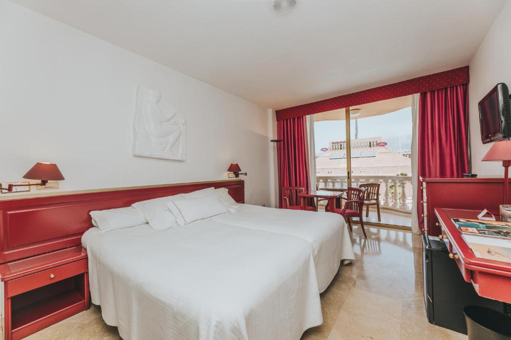 Mūsdienīga viesnīcas numuriņa iekārtojums ar divām gultām, sarkaniem akcentiem un balkonu, no kura paveras skats uz ārpusi. Numurā ir televizors un neliels galds ar krēsliem.