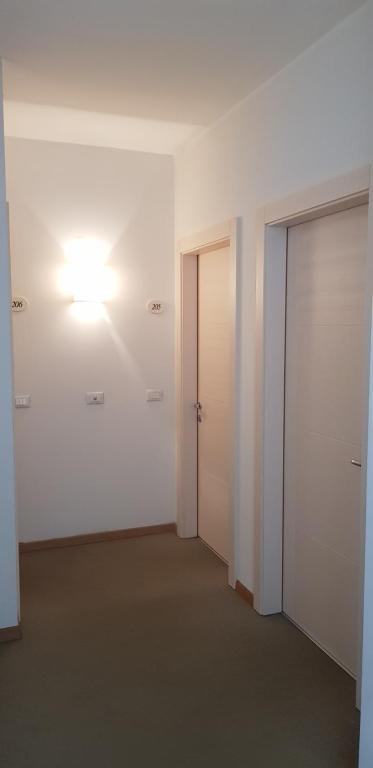 Gaišs un moderns koridors ar divām durvīm un siena lampu, kas nodrošina patīkamu apgaismojumu. Uz sienas redzami numuri.