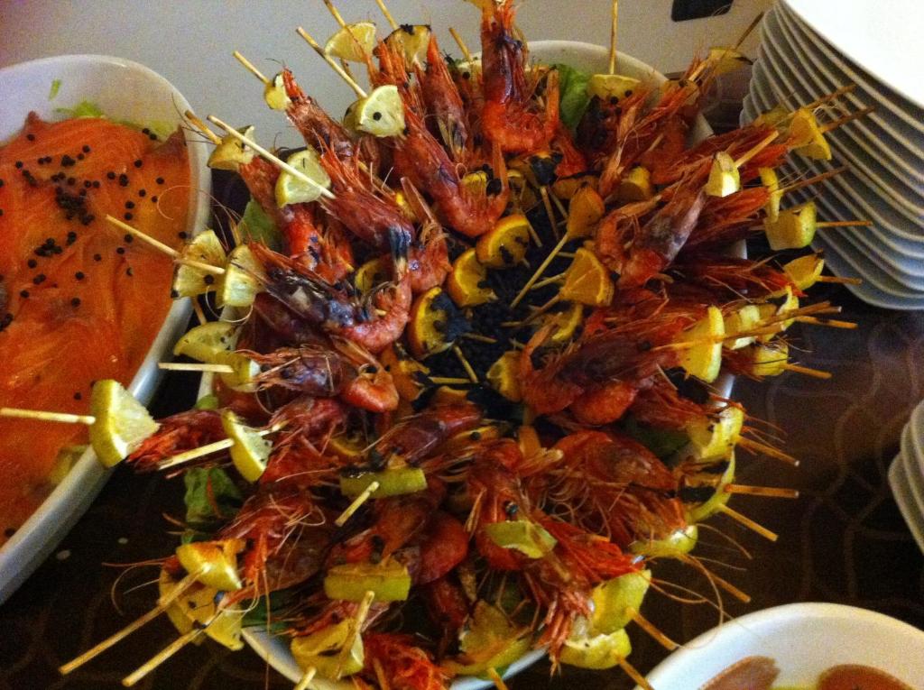 Garšīgi garneles uz iesma ar citronu šķēlītēm, pasniegtas uz dārzeņu gultas. Blakus redzama lasis.