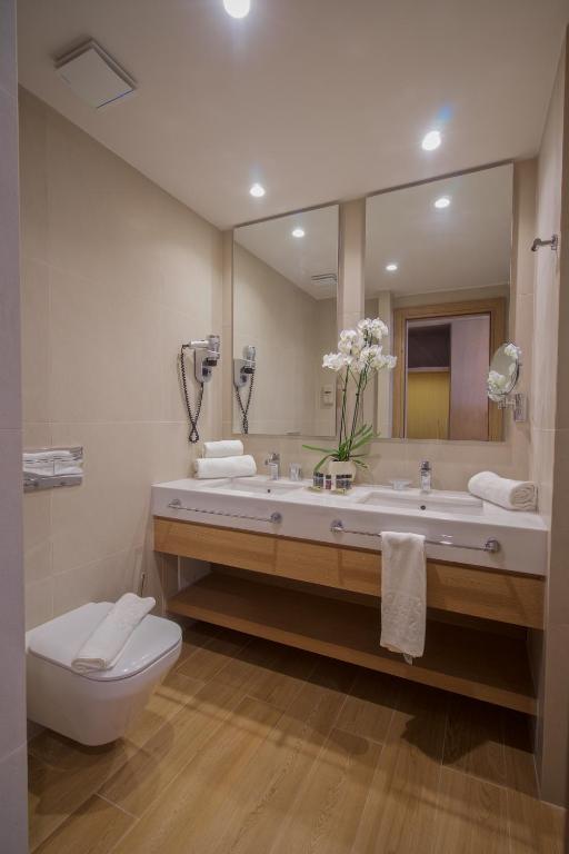 Moderns vannas istabas interjers ar koka izlietni, spoguļiem un ziedu kompozīciju. Vannas istaba ir gaiša un eleganta, ar mūsdienīgu apgaismojumu.