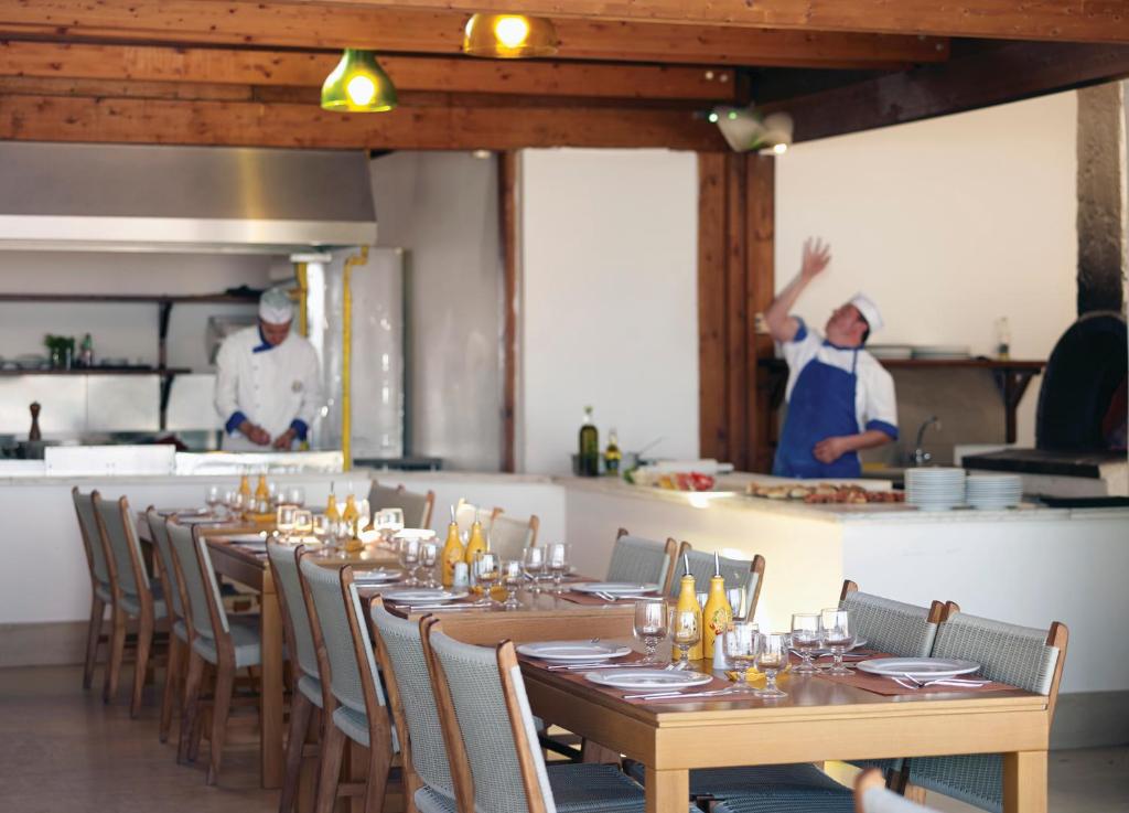 Restorāna iekšiene, kurā redzami pavāri, kas strādā virtuvē, un elegantas galdiņu klāšanas detaļas. Gaisotne ir mājīga un viesmīlīga, piedāvājot patīkamu ēdināšanas pieredzi.