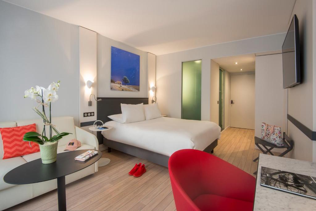 Mūsdienīga viesnīcas istaba ar plašu gultu, dīvānu un elegantu interjeru. Istabā ir glezna uz sienas, televizors un maza kafijas galdiņa zona.