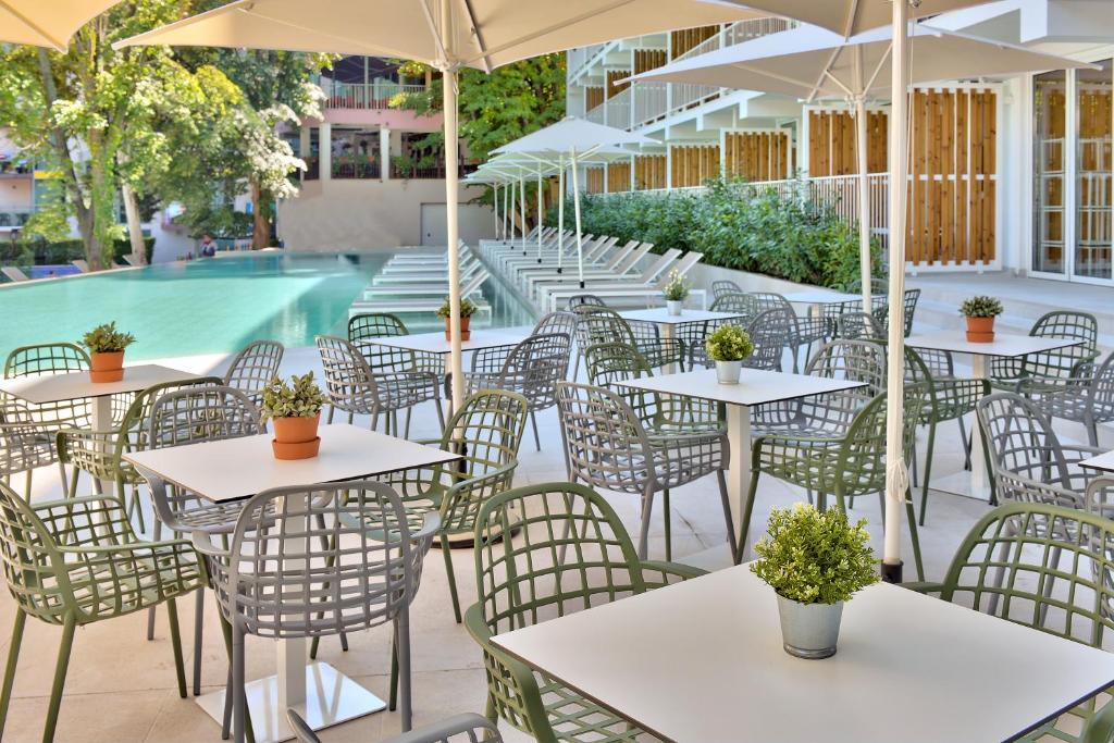 Moderns terases dizains ar galdiem un krēsliem blakus baseinam, zaļas augu kompozīcijas uz galdiem un saulessargi. Ideāls vieta relaksācijai un atpūtai.