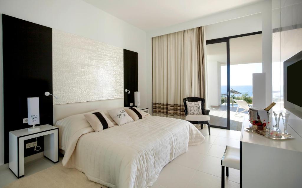 Mūsdienīgs viesnīcas numurs ar elegantu interjeru, kurā ir liels gulta, melnbalts dizains un skats uz jūru. Logi ļauj ienākt dabiskajai gaismai, radot patīkamu atmosfēru.