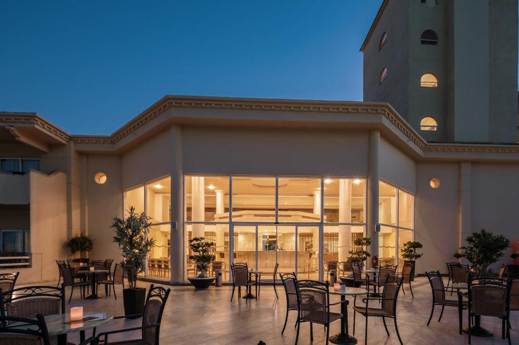 Mūsdienīga ēka ar plašu stiklotu fasādi un āra terasi, kurā izvietotas galdi un krēsli, radot patīkamu atmosfēru vakara relaksācijai. Apsmidzināti zaļumi papildina ainavu.