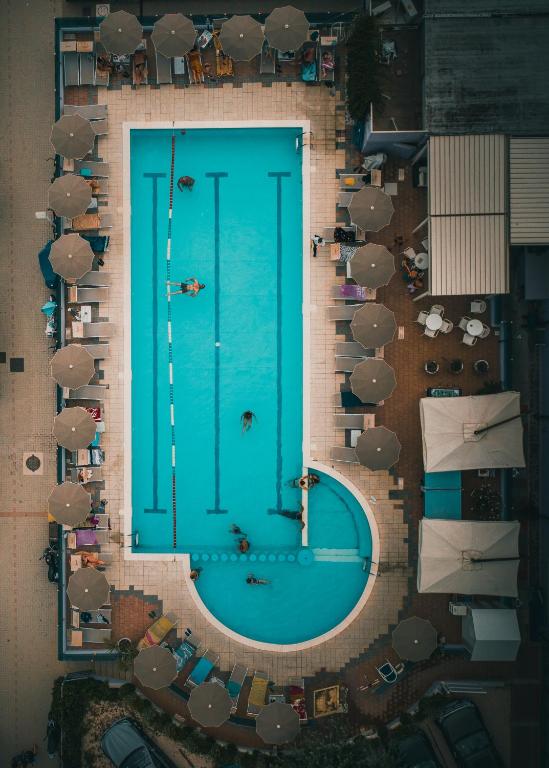 Baseins ar zilu ūdeni un saulessargiem ap to, redzams no augšas, kur cilvēki atpūšas un peld.