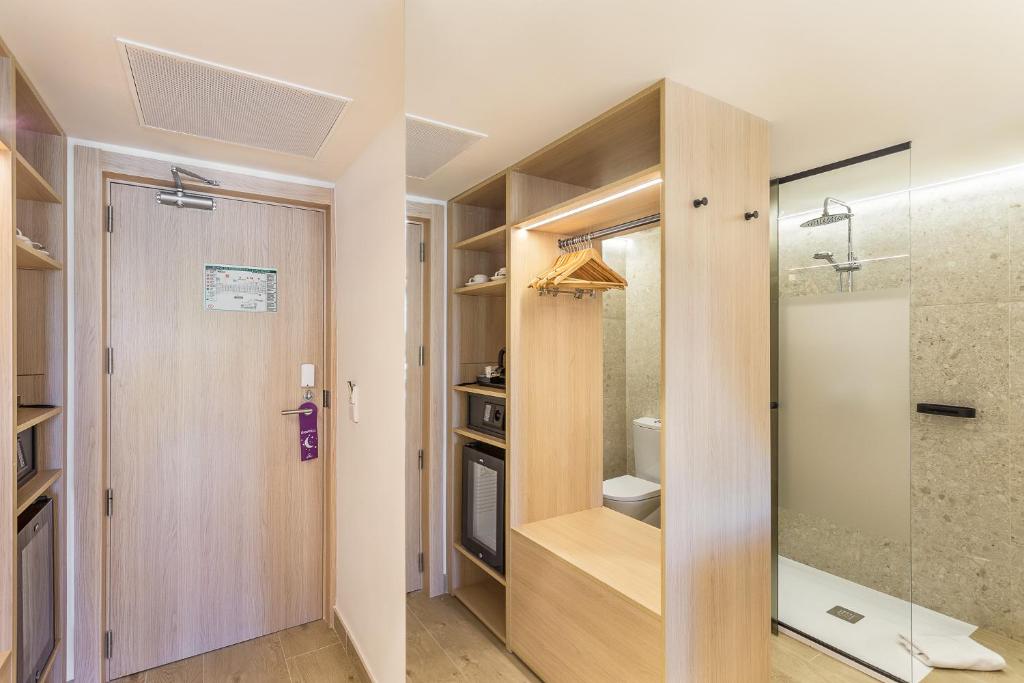 Moderns viesnīcas numurs ar koka mēbelēm, apgaismojumu un stikla dušas kabīni. Interjers ir gaišs un funkcionāls, radot komfortablu atmosfēru.