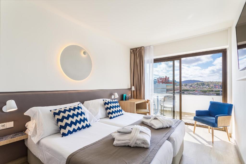 Mūsdienīgs viesnīcas numurs ar divām gultām, zilu un baltu spilvenu, kā arī ērtu atpūtas krēslu pie loga. Numurā ir gaišs interjers un skats uz ārpusi.