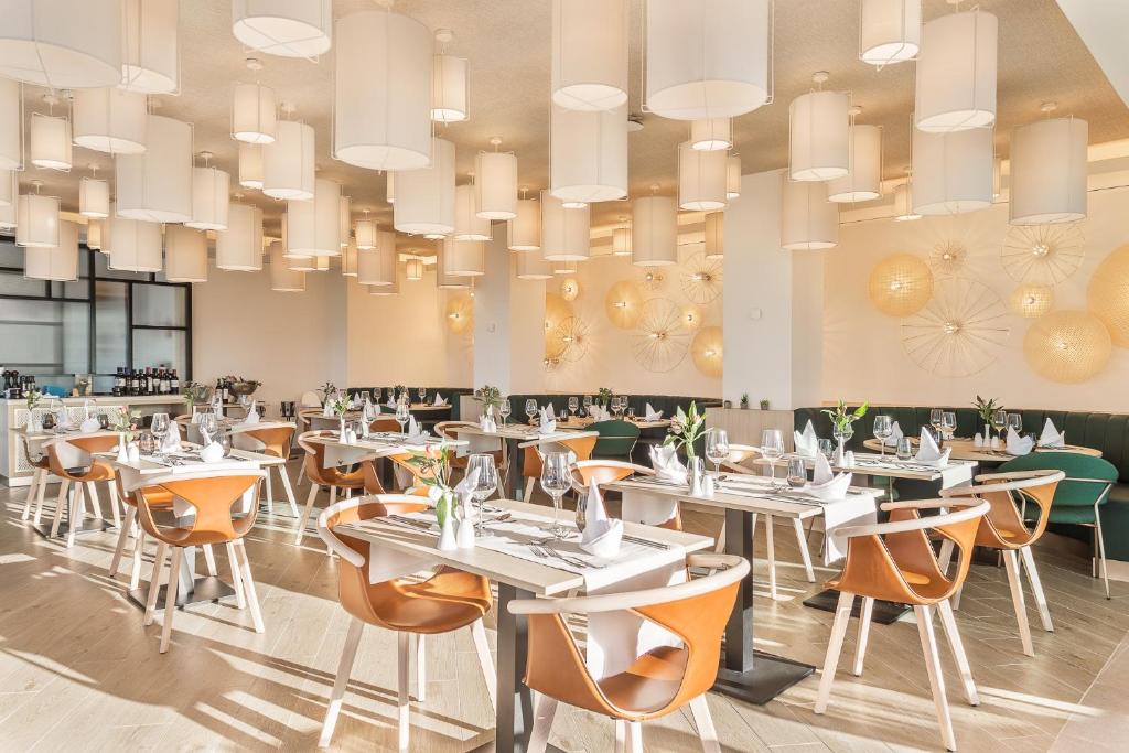 Mūsdienīgs restorāns ar elegantu interjeru, kurā ir eleganti galdi un gaismas ķermeņi. Telpā redzami ērti krēsli un dekoratīvi elementi, kas rada patīkamu atmosfēru.