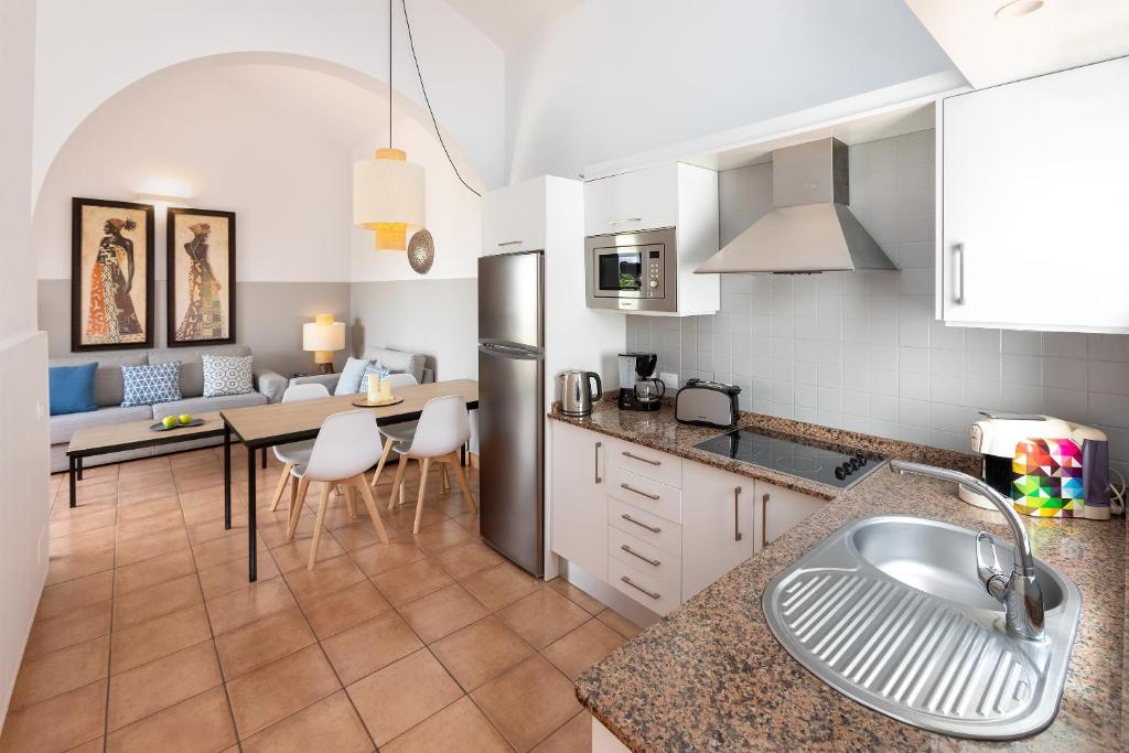 Mūsdienīga virtuve ar atvērtu plānojumu, iekārtota ar modernām ierīcēm un ērtu ēdamgaldu. Interjers ir gaišs un viesmīlīgs, ar stilīgu apgaismojumu un mākslas darbiem uz sienām.