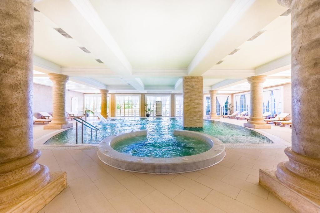 Luksusa spa telpa ar iekštelpu baseinu un atpūtas zonu, piedāvājot mierīgu atmosfēru un relaksāciju. Eleganti kolonnas un gaišas krāsas rada patīkamu vidi.