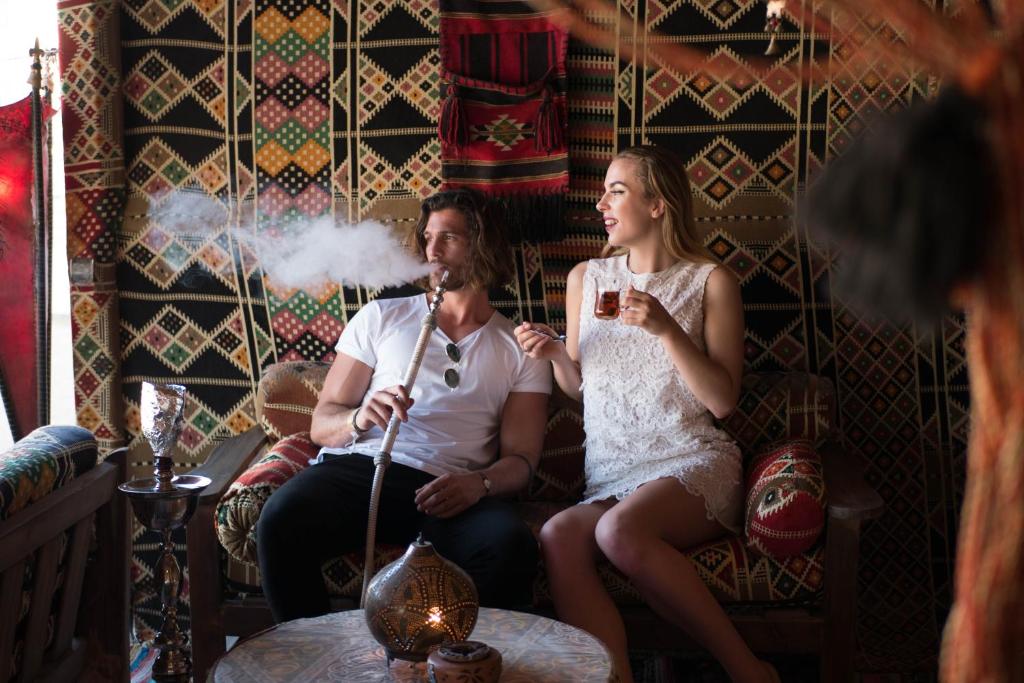 Pāris relaksējas ērti iekārtotā telpā, baudot šašliku un tēju, kamēr ap viņiem ir krāsainas auduma sienas un tradicionālas dekorācijas.