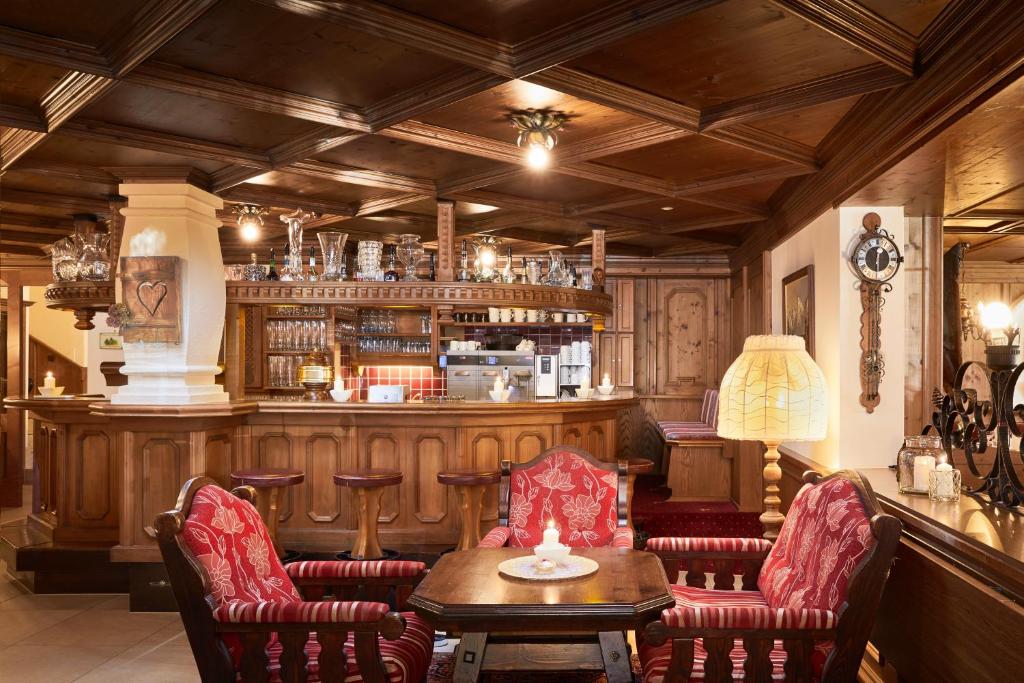 Elegants kafejnīcas interjers ar koka apdari, sarkaniem krēsliem un koka bāru. Gaisma rada mājīgu atmosfēru, ideālu relaksācijai.