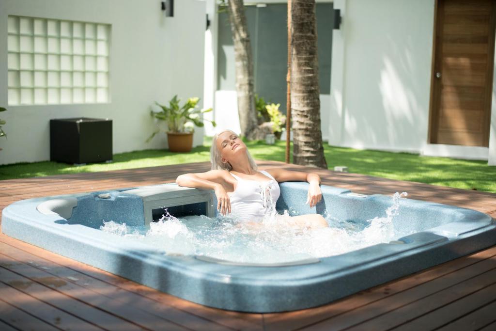 Sieviete relaksējas džakuzi, baudot sauli un ūdens burbuļus, apkārt zaļojoši augi un mūsdienīgs interjers.