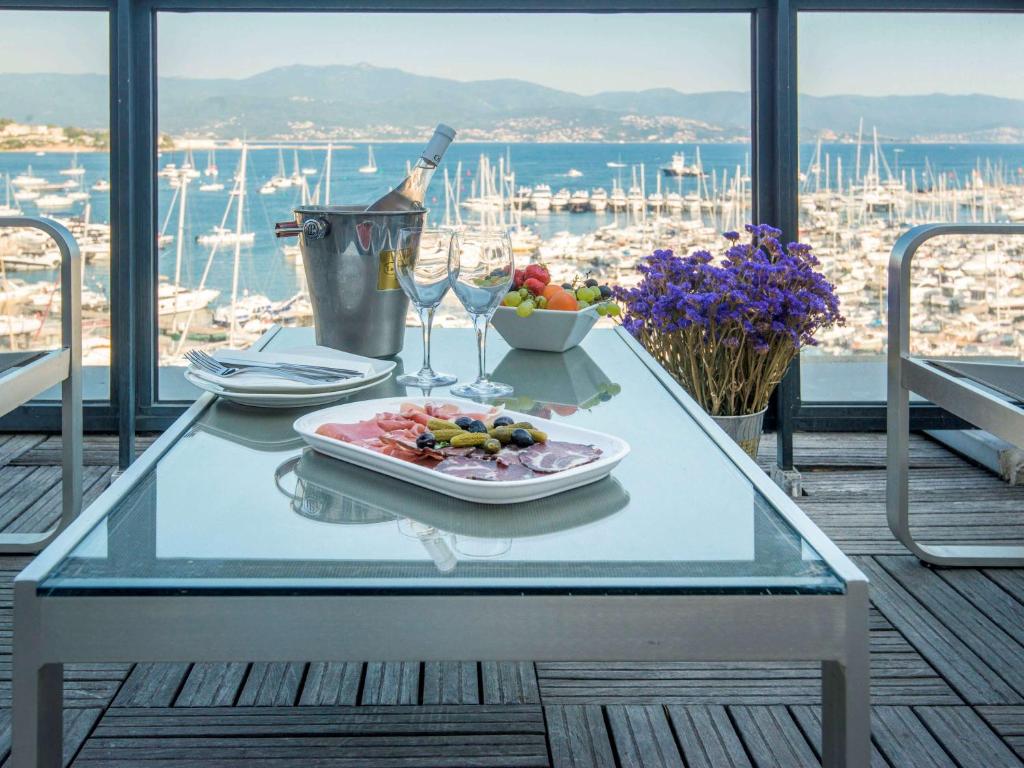Elegantā terase ar skatu uz jūru, uz galda ir pasniegti delikāti ēdieni, augļi un dzirkstošais vīns. Ziedi pie galda piešķir gaisotni.