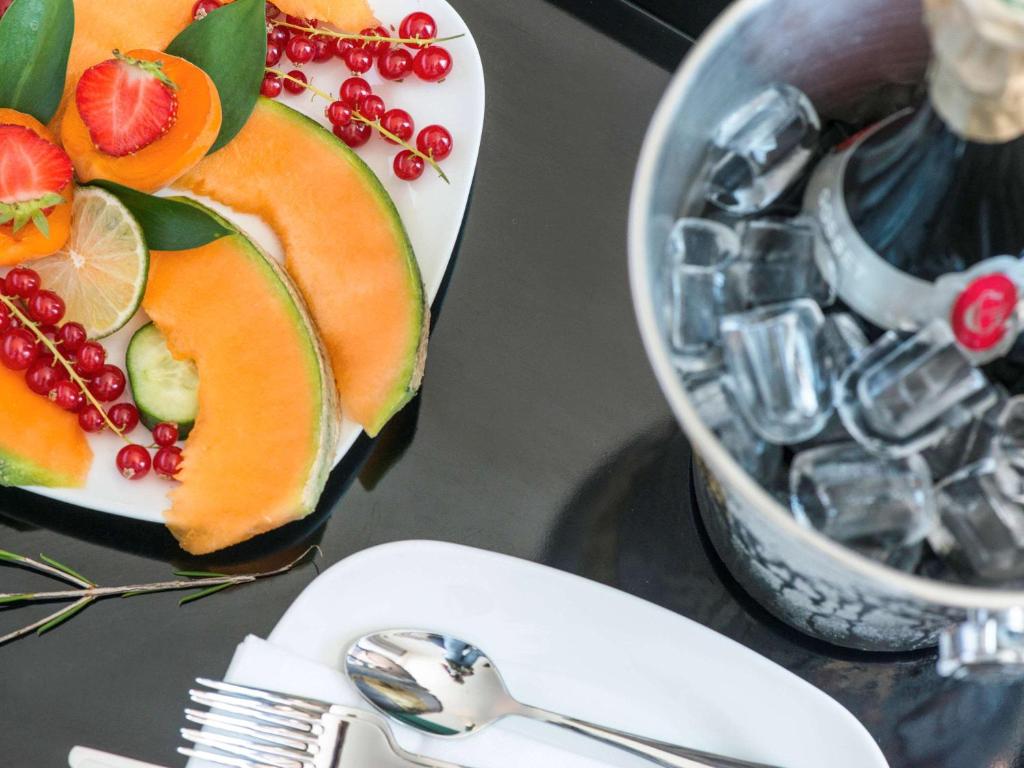 Svaigu augļu šķīvis ar meloni, zemenēm un jāņogām, blakus ledus spainis ar šampanieti, uz elegantas galda virsmas.