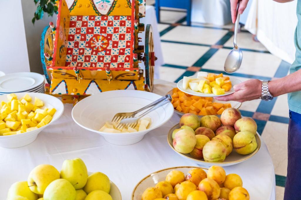 Svaigu augļu bufete ar dažādām šķirnēm, tostarp ananāsiem, melones un persikiem, uz galda. Aiz galda ir krāsains rotājums, kas piešķir svinīgu atmosfēru.
