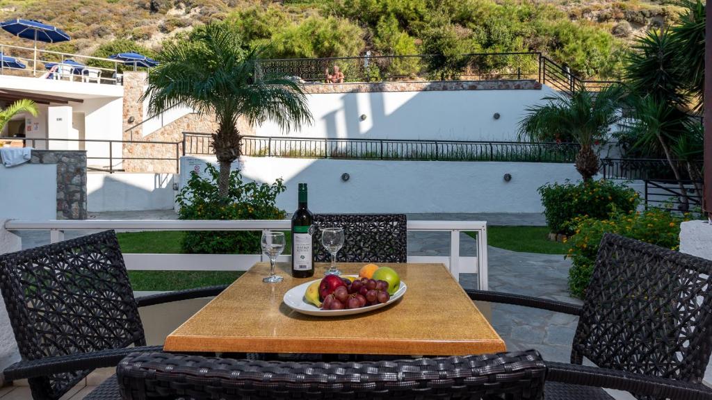 Dārza terase ar galdu, uz kura atrodas augļu trauks un pudele vīna, apzaļumota vide ar palmām un ziediem. Ideāla vieta relaksācijai un baudīšanai.