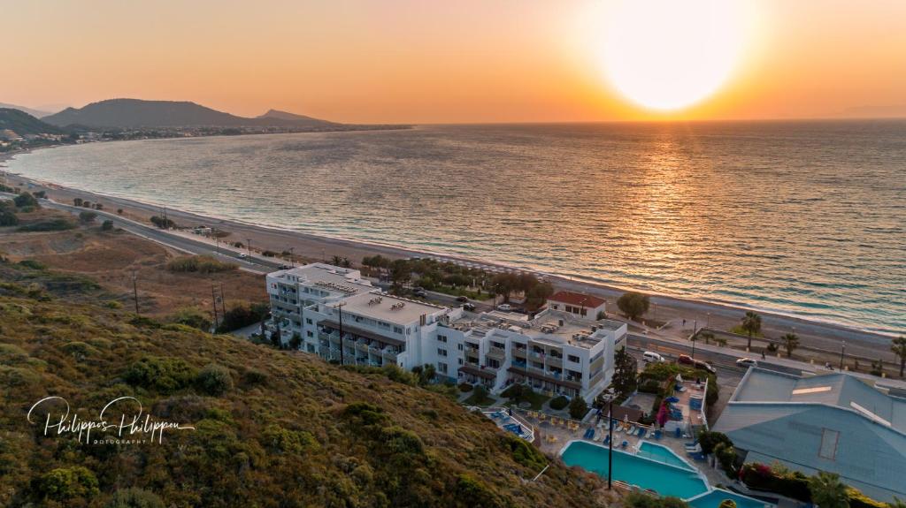 Saulriets virs jūras ar viesnīcu un pludmali, kas izskatās mierīga un relaksējoša. Ainava atspoguļo dabu un atpūtu pie ūdens.