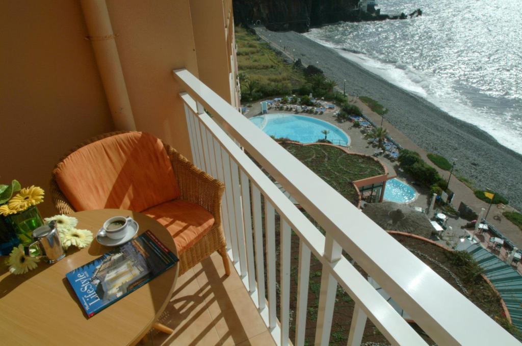 Balcony view featuring a cozy orange chair, a small table with coffee and flowers, overlooking a serene beach and swimming pools. Perfect spot for relaxation.