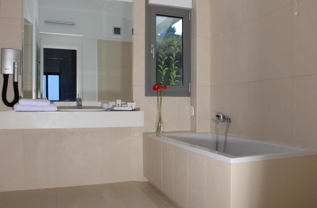 Mūsdienīgs vannas istabas interjers ar vannu, spoguli un logu, kas piedāvā dabisku apgaismojumu un skatu uz dabu. Vannas istabā ir arī dvieļi un higiēnas piederumi.