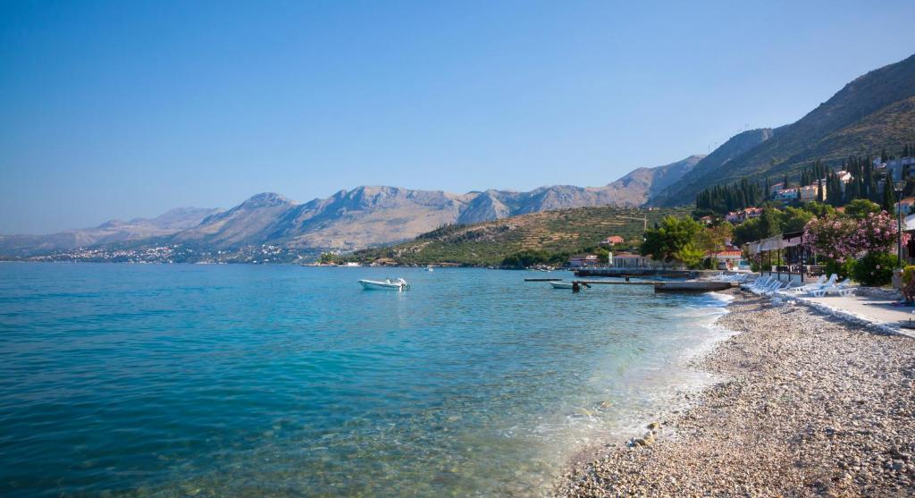Skaista pludmale ar akmeņainu krastu un skaidru ūdeni, ap kuru stiepjas kalnu ainava un nelieli kuģi. Pavasara ziedi rotā tuvumā esošos kafejnīcas un mājas.