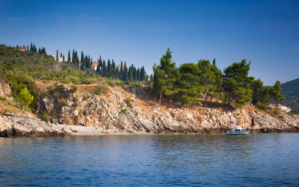 Piedāvā skaistu ainavu ar klintīm, priežu kokiem un mierīgu jūru, kurā redzama laiva. Šis attēls rada relaksējošu atmosfēru un atspoguļo dabu.