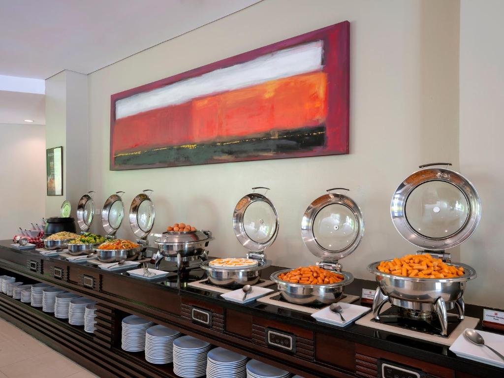 Bufete ar dažādiem dārzeņu un augļu ēdieniem, kas pasniegti stilīgās metāla traukos, fona sienas glezna ar siltām krāsām.