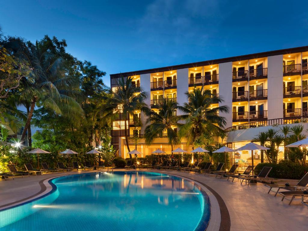 Peldbaseins ar apgaismotu viesnīcu fonā, apkārt palmām un sauļošanās krēsliem, radot relaksējošu atmosfēru. Ideāla vieta atpūtai un atpūtas baudīšanai.